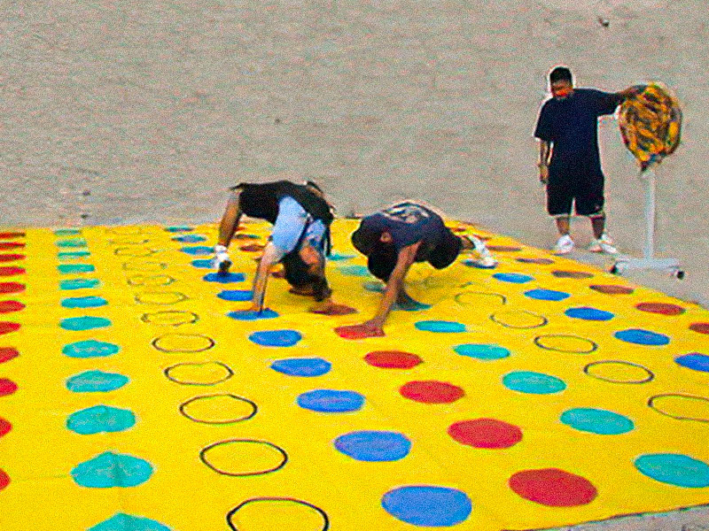 People in different positions, trying to keep their hands and feet on the correct colored circles playing a giant game of Twister.
