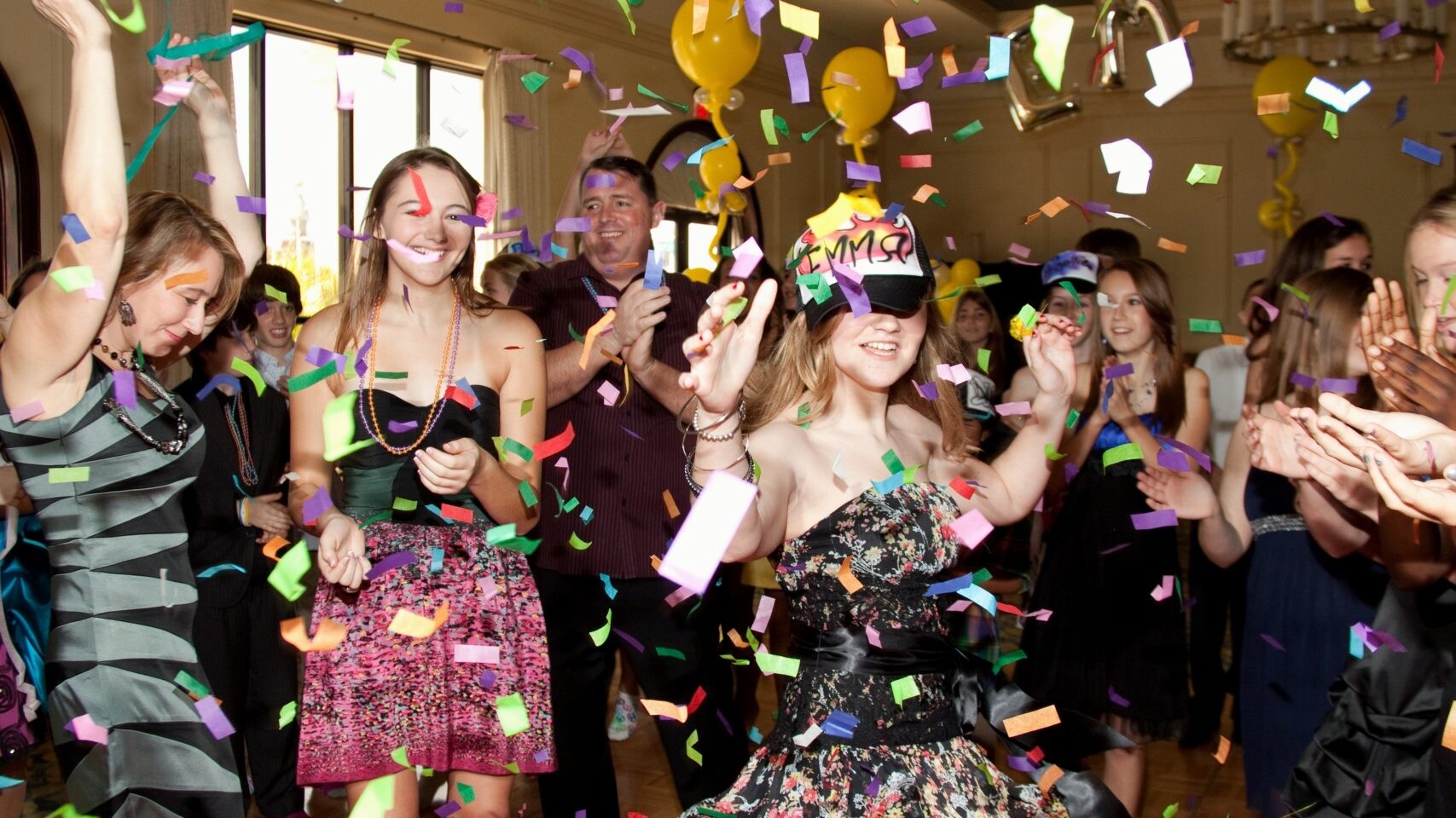 Girls smiling, clapping, dancing, and having fun at a party with confetti falling for a bar mitzvah event.