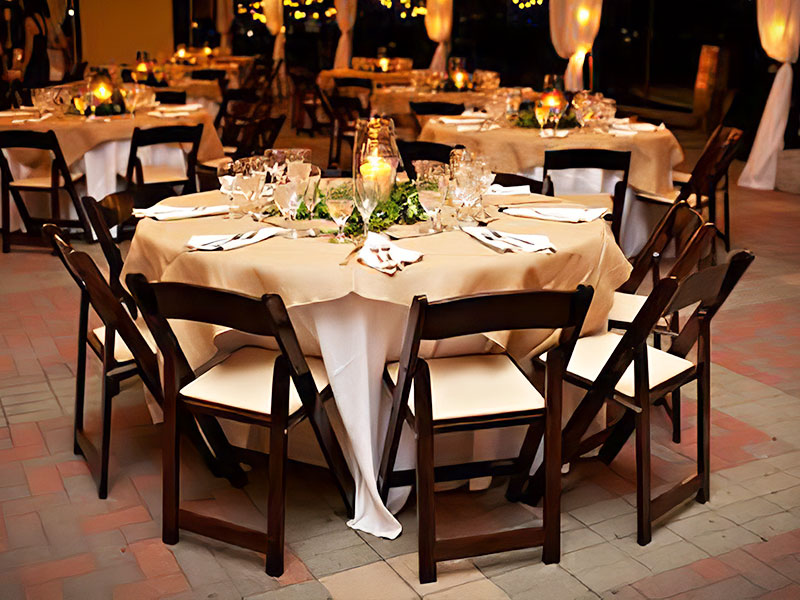 Large round table with eight brown and tan wooden chairs set with a white and tan table cloth for a nice wedding.