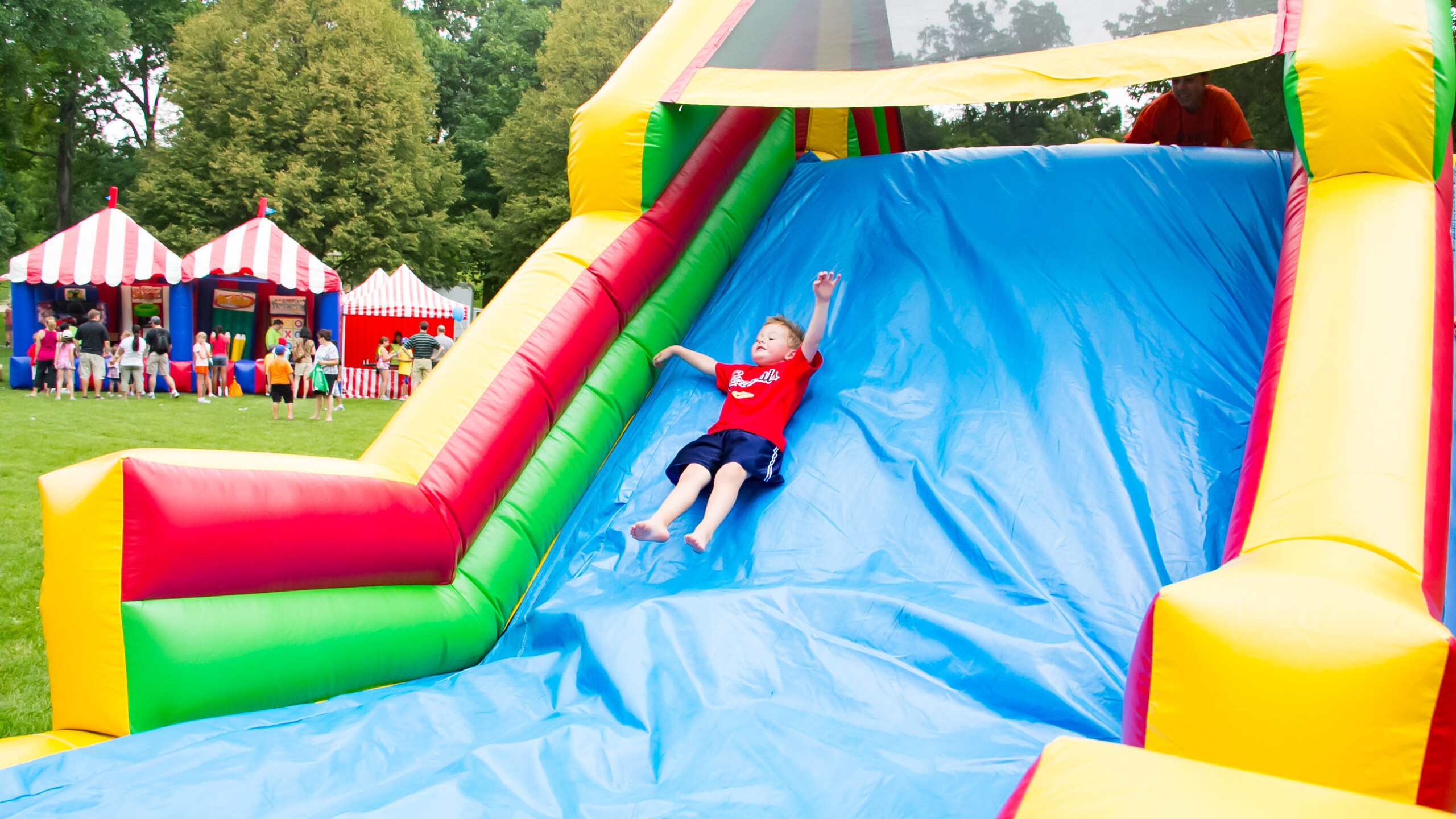 A kid closing his eyes as he slides down an inflatable slide at a festival.
