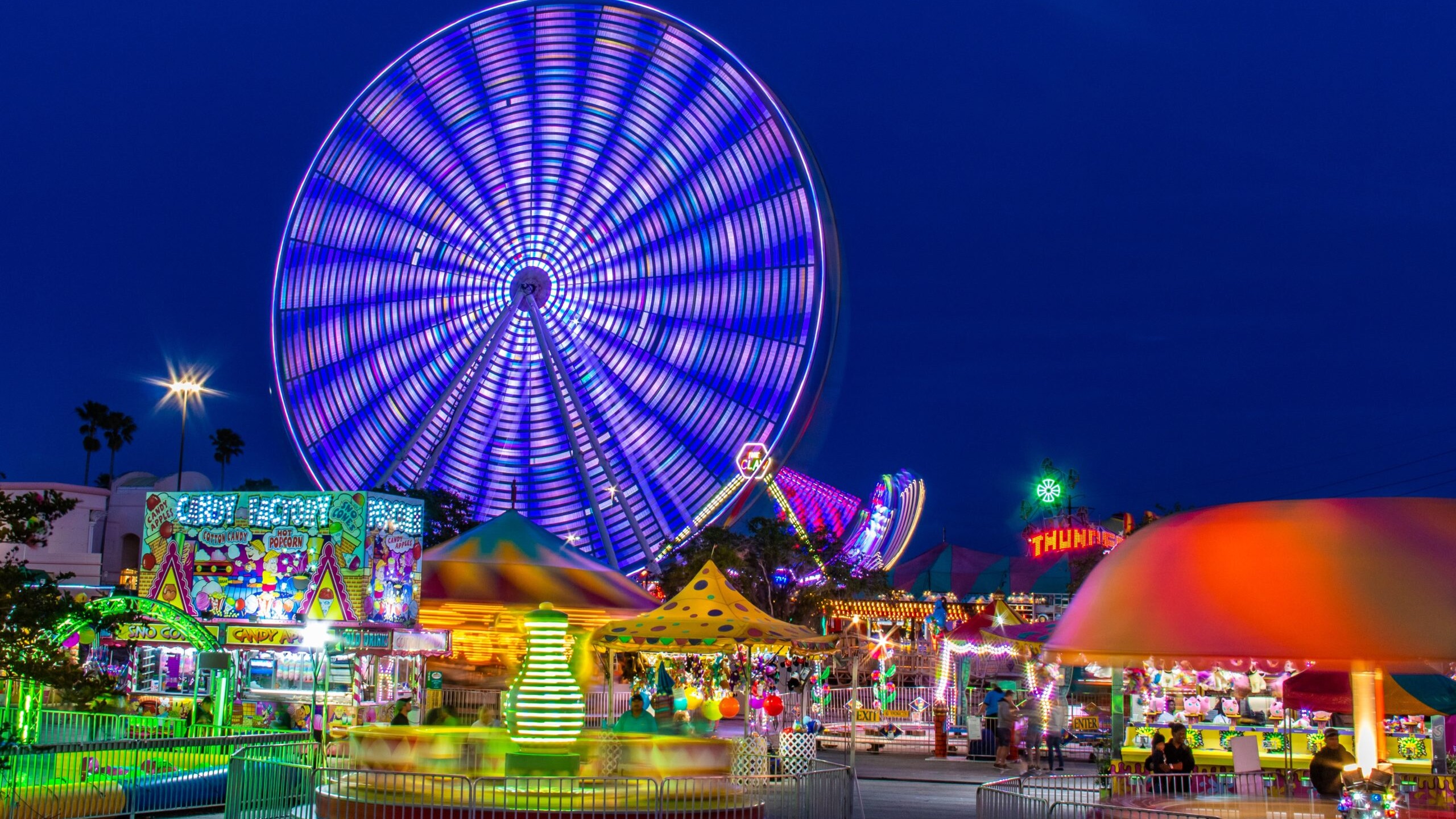 Amusement park rides and Faris wheel at night with fast moving neon lights