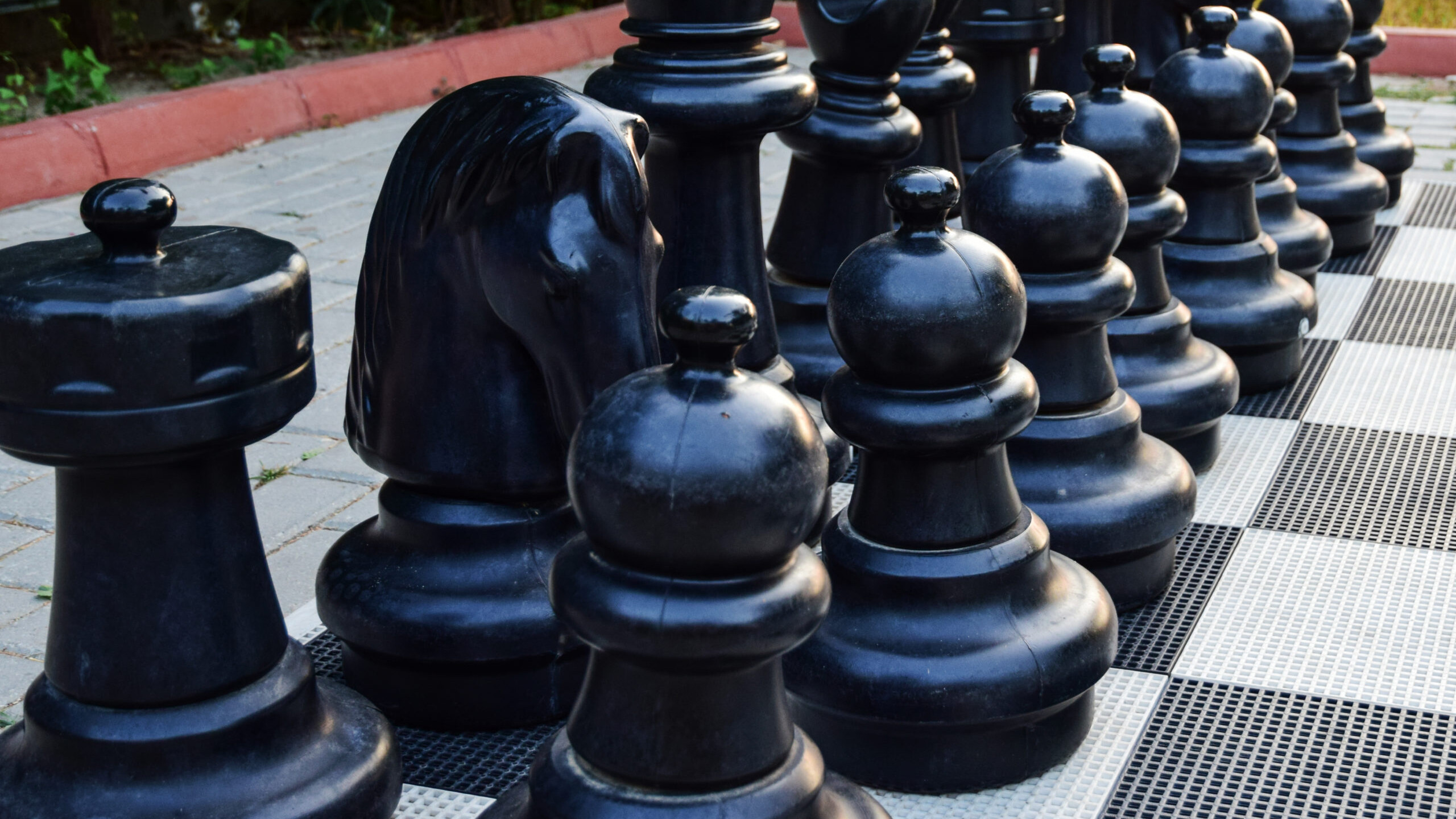 Life size chess game pieces set up outside on a checkered chess floor.