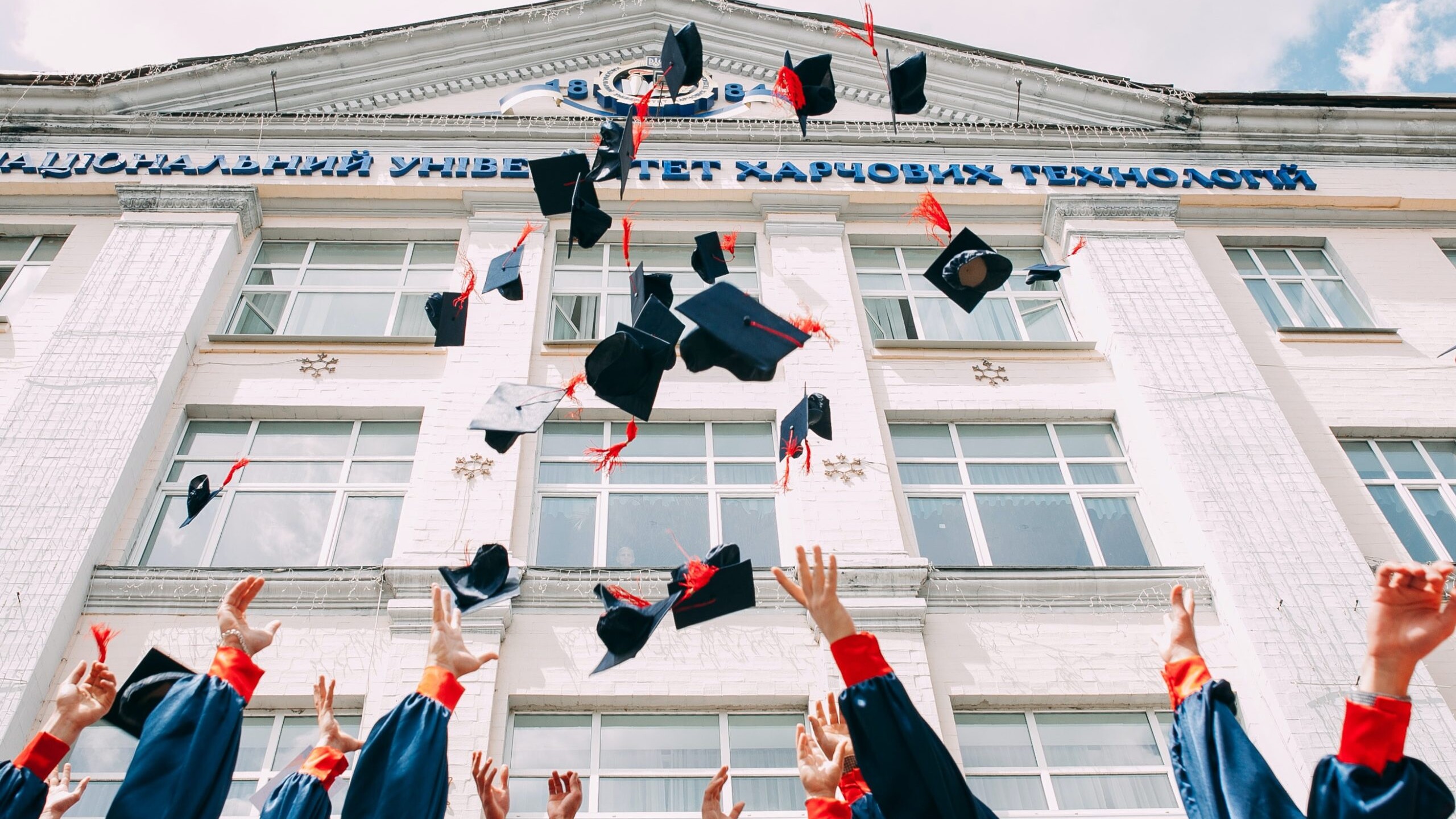 Kids throwing graduation hats Infront of a school for a graduation party event.