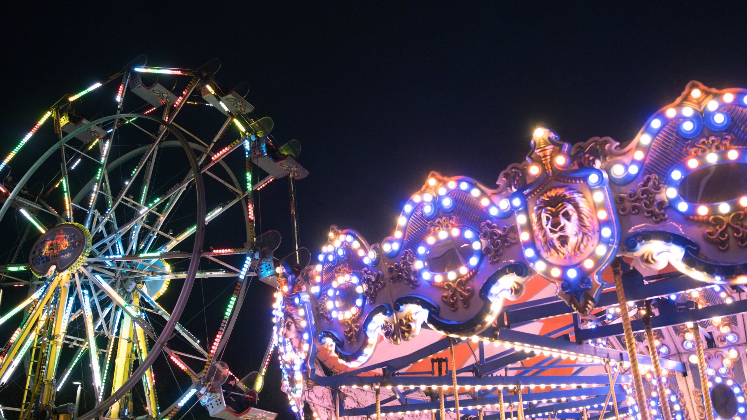 A fairs wheel, and carousel with neon lights at night at a carnival, festival event.