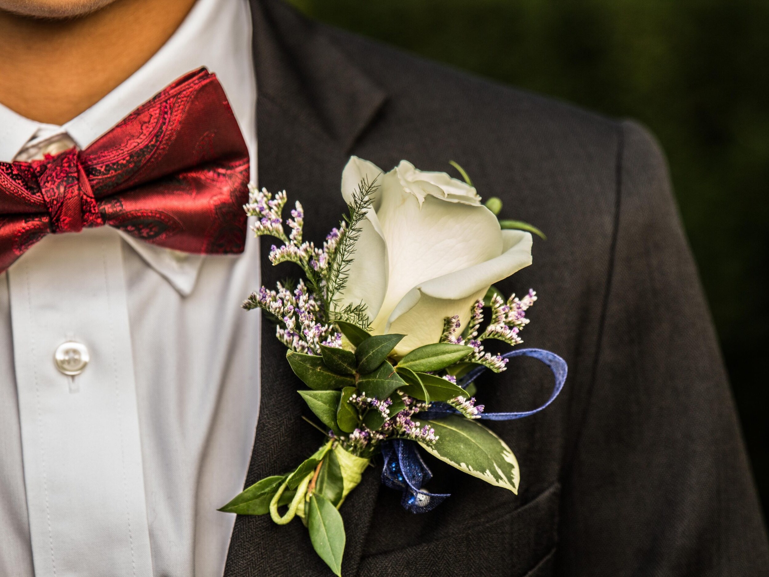 A boutonniere on a black suit next to a red bowtie.