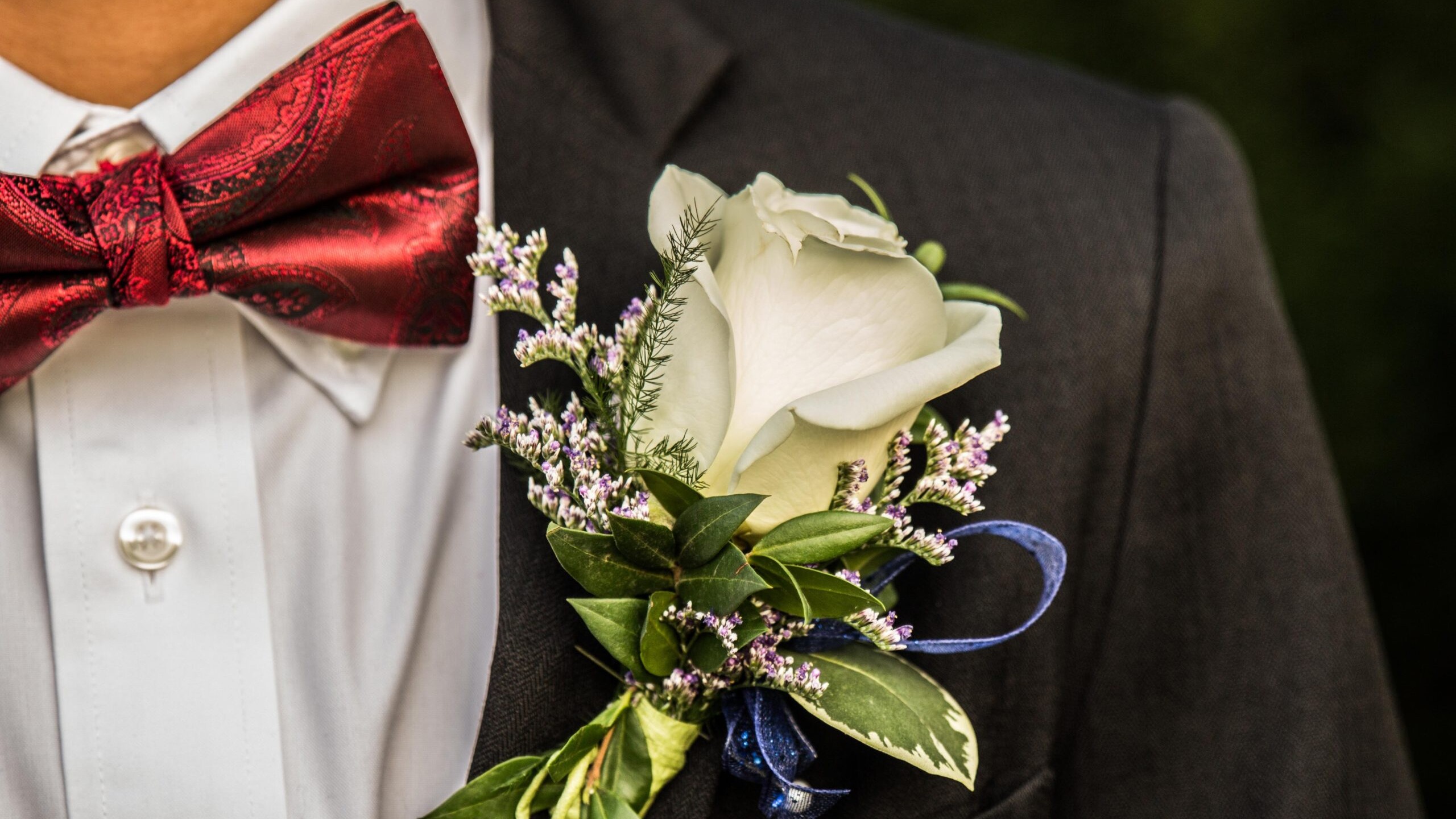 A boutonniere on a black suit next to a red bowtie.