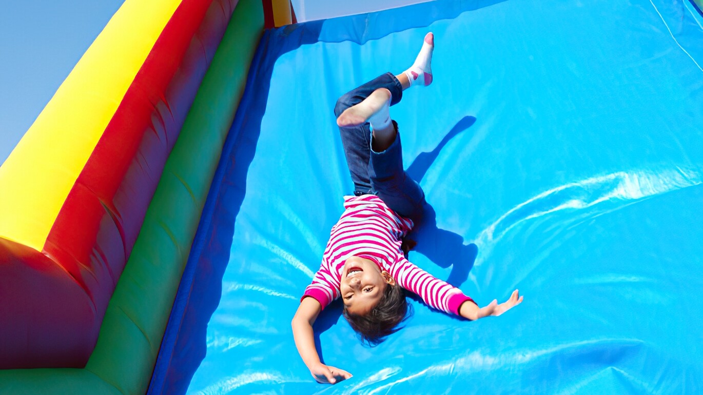 A girl upside down smiling and having fun sliding down an inflatable slide.