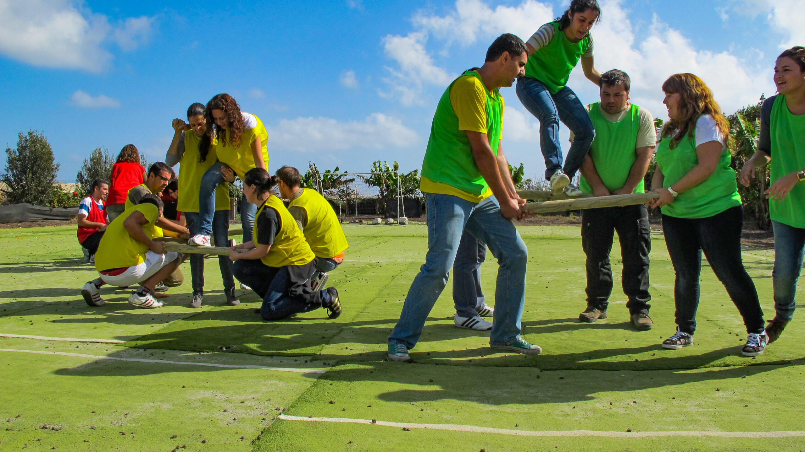 A group of people wearing green playing a team building game on a green field