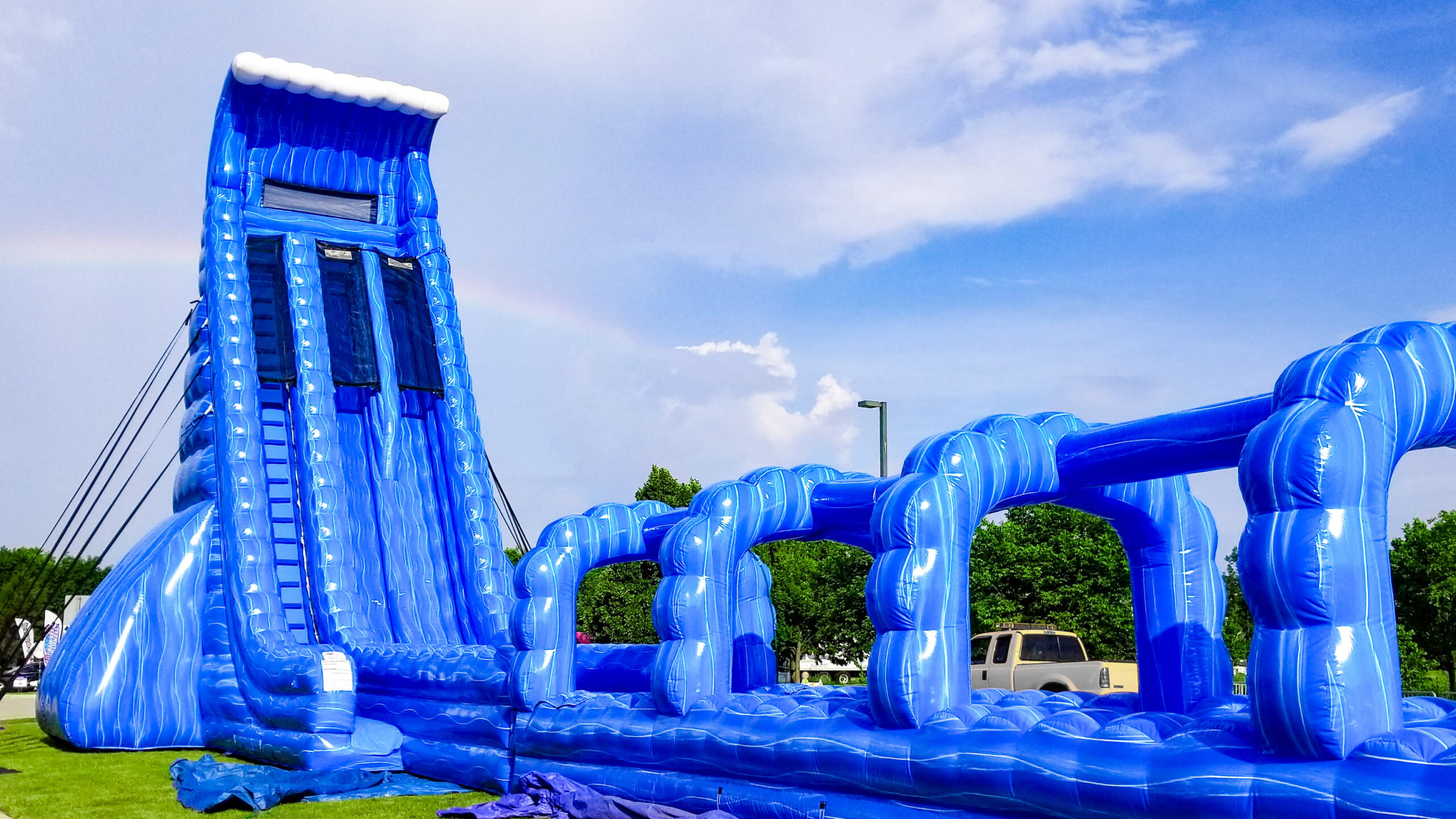 Massive blue and white title wave inflatable water slide with slip-n-slied and pool on a hot sunny summer day for a party.