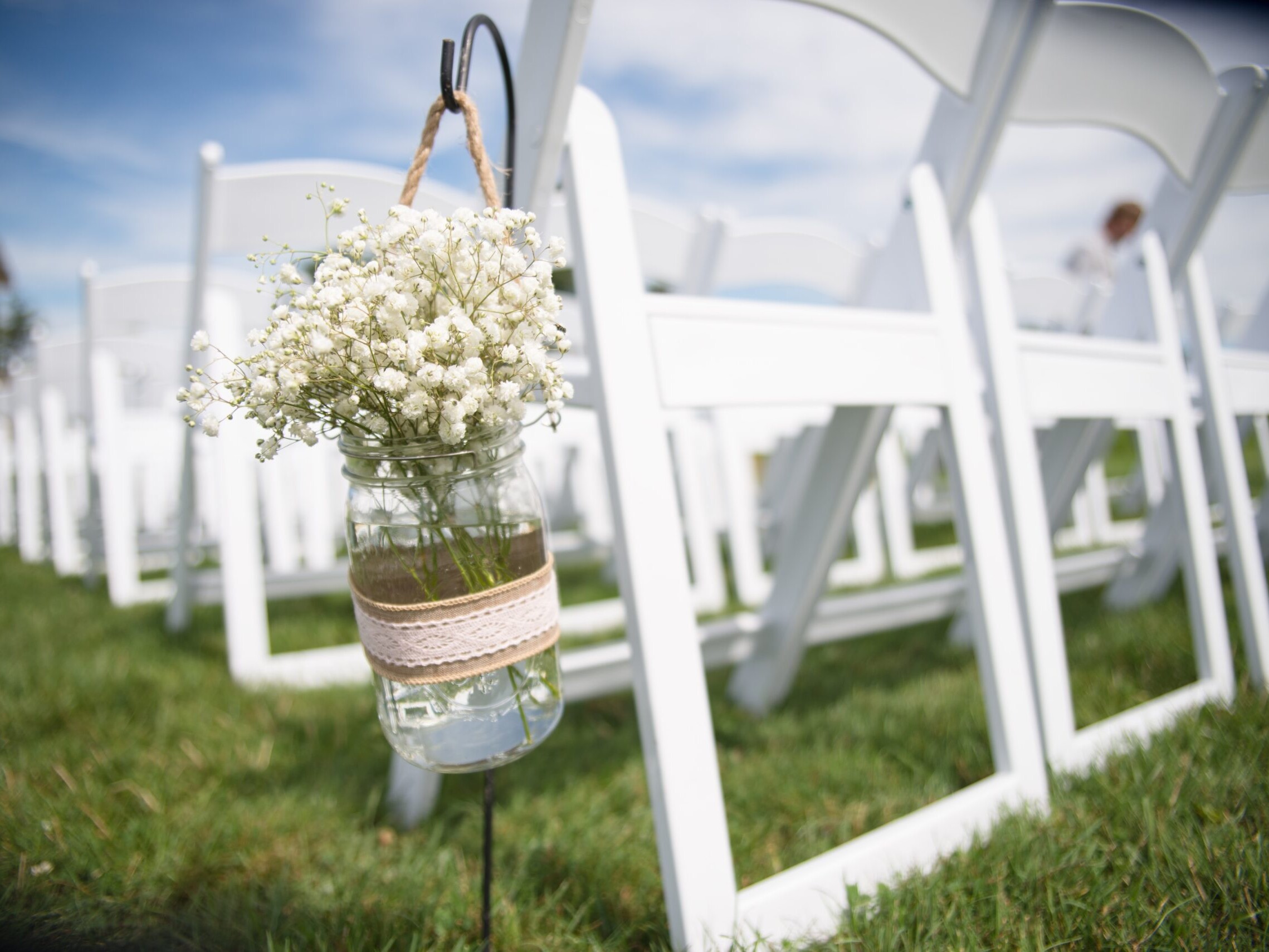 White chairs lined up for a wedding with a glass jar of flowers.