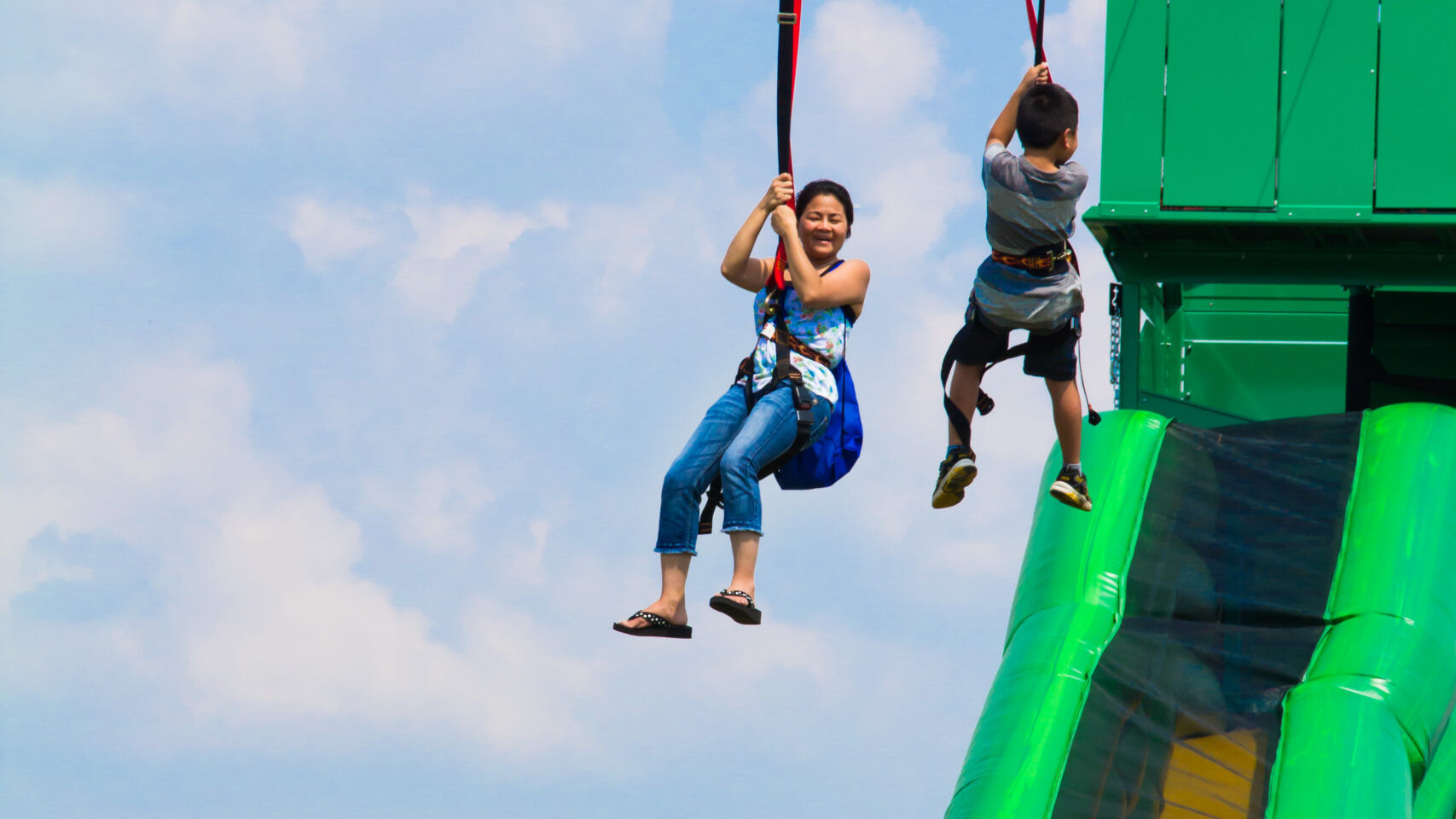 A mom and kid having fun riding down a mobile zip line with slide rental.