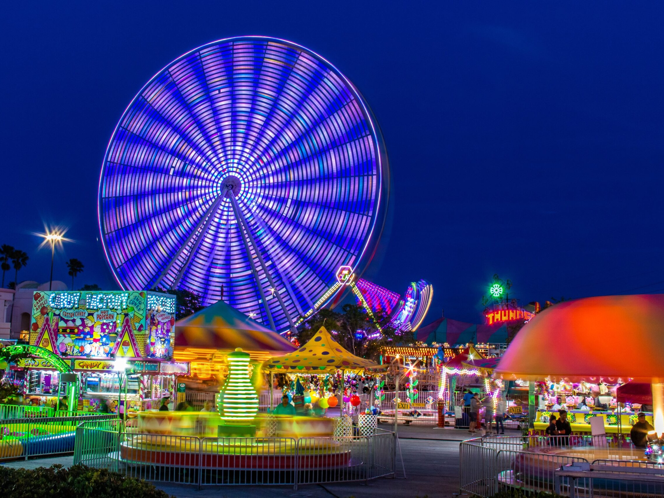 Amusement park rides and Faris wheel at night with fast moving neon lights